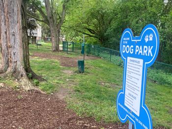 a blue sign in a park with a dog park in the background